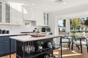 A modern kitchen with white cabinets, a central island, and a dining area with chairs. - Luxury Oasis, 3min to Oldtown! 4bd4Ba HtdPool&Spa! (Scottsdale)