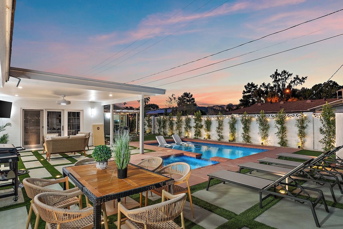 A backyard with a swimming pool, lounge chairs, a dining table, and a covered patio area.