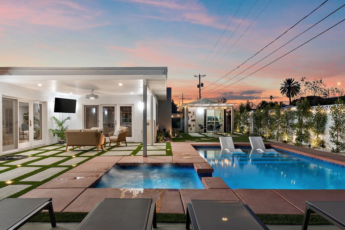 A modern outdoor pool area with a clear sky, a covered seating area, and a well-maintained lawn.
