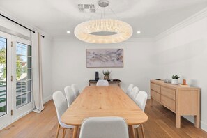 Ein Esszimmer mit Holztisch, weißen Stühlen, einer Pendelleuchte, einem Gemälde und einem Schrank.