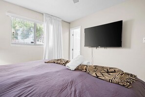 A bedroom with a bed, a television mounted on the wall, a window with curtains, and a door. - Scottsdale Old Town Lewis 🌵⛳ Private Hot Tub Near Old Town & the Zoo (Scottsdale)