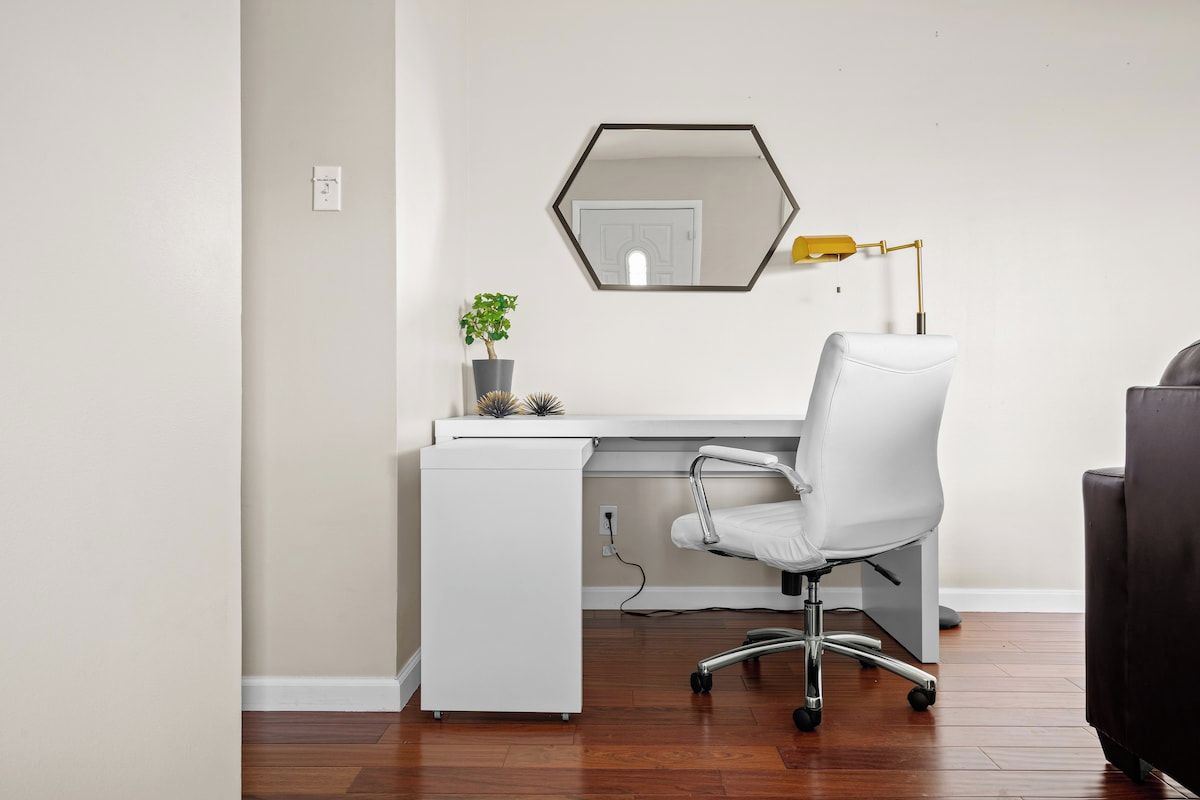 A modern office space with a white desk, a white office chair, a hexagonal mirror, and a yellow desk lamp.