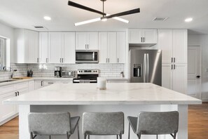 A modern kitchen with white cabinetry, a central island with bar stools, stainless steel appliances, and a ceiling fan. - Scottsdale Andora Retreat 🌵⛳ Heated Saltwater Pool Near Kierland Commons (Phoenix)