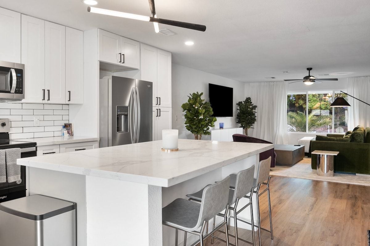 Una cocina moderna con armarios blancos, electrodomésticos de acero inoxidable y una isla grande con taburetes de bar.