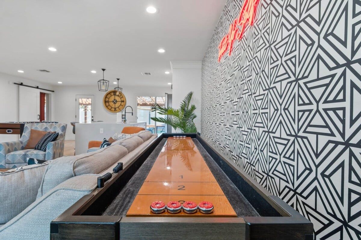 A shuffleboard table in a modern living room with a geometric patterned wall and a clock.