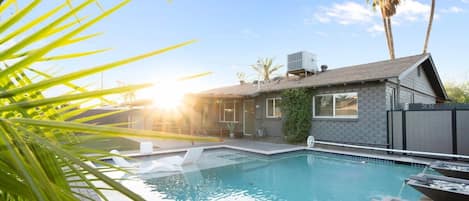 A swimming pool with a house in the background, surrounded by palm trees.