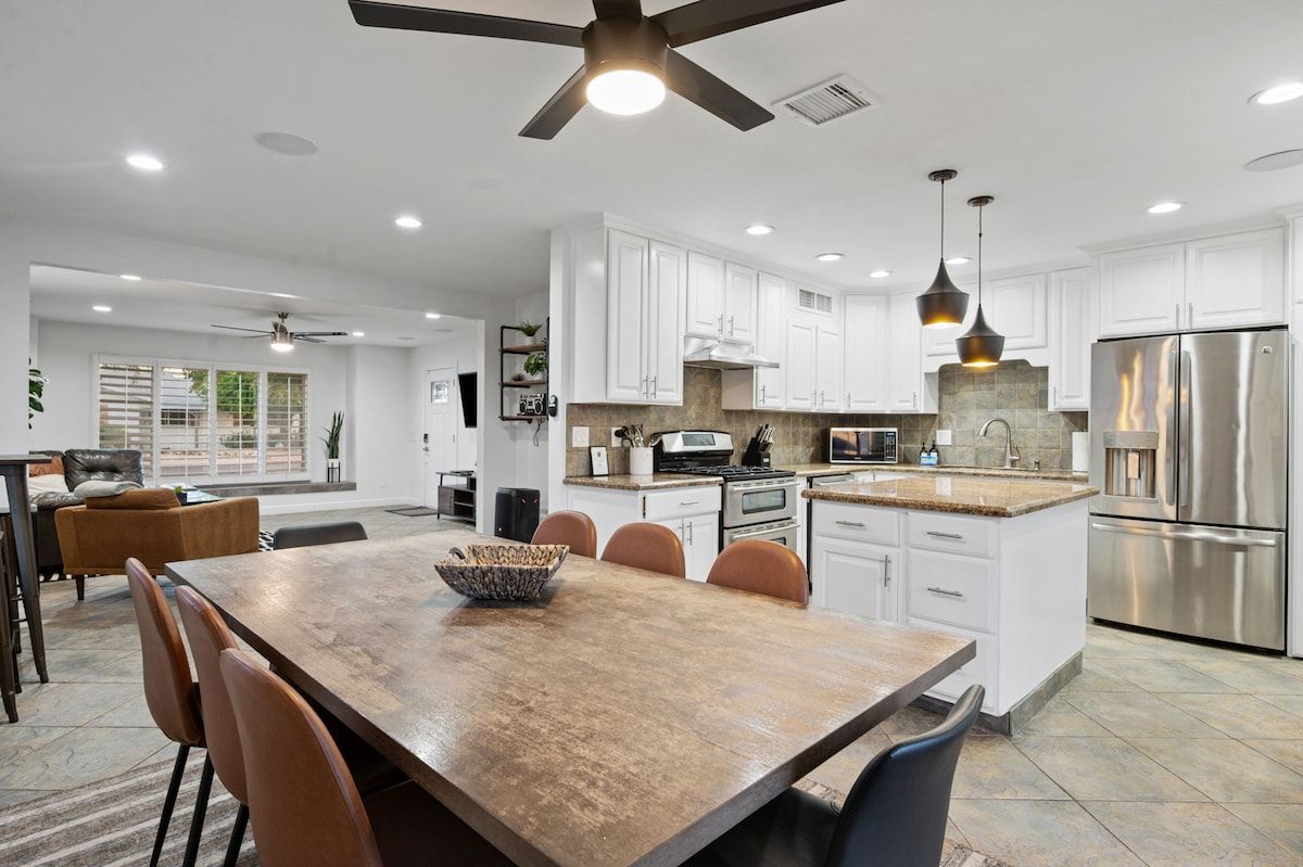 A modern kitchen with white cabinets, stainless steel appliances, and a dining area with a wooden table and chairs.