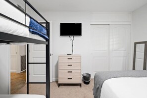 Un lit superposé avec une serviette bleue, un téléviseur fixé au mur, une commode et une porte.