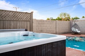 Un jardin avec un jacuzzi et une piscine, entouré d’une clôture en bois et d’un mur en briques.