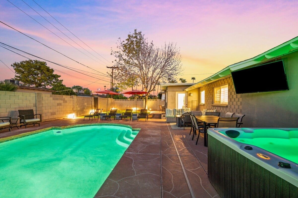A swimming pool with lounge chairs and a hot tub in a backyard setting.