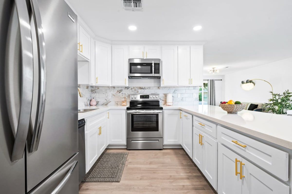 A modern kitchen with stainless steel appliances, white cabinetry, and a marble backsplash.