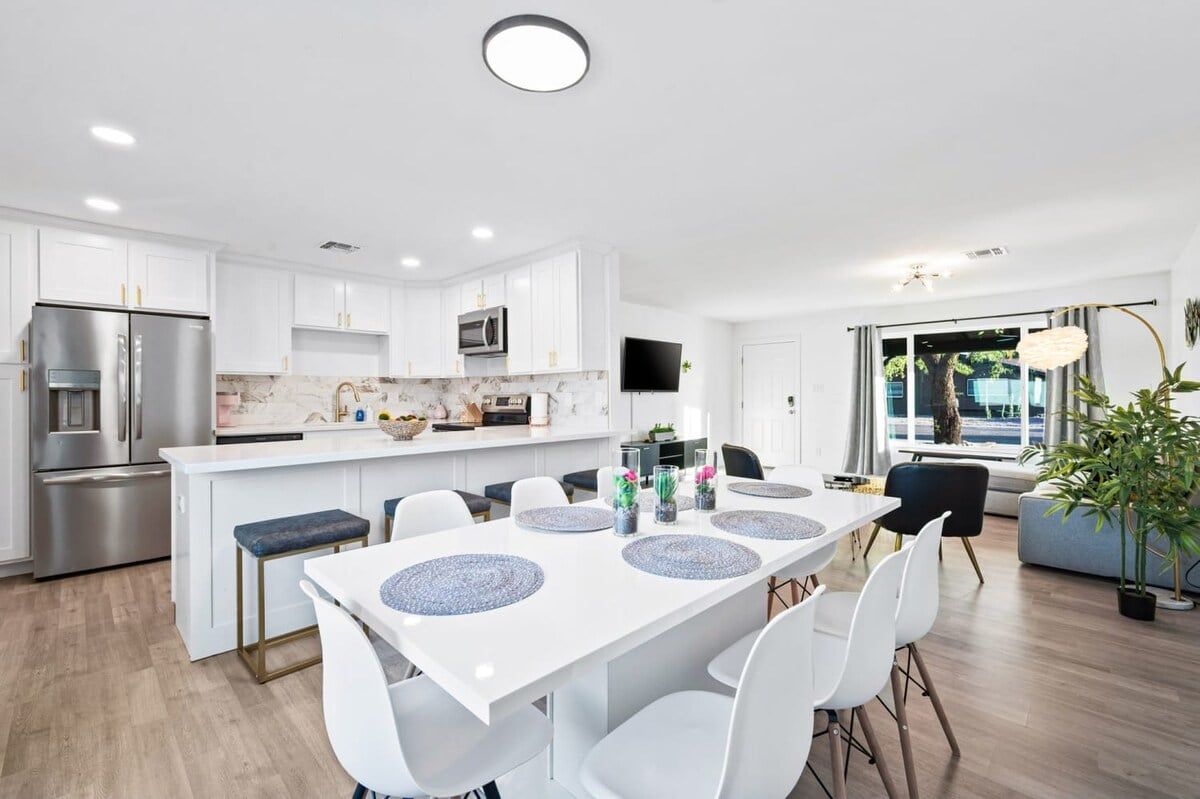 A modern kitchen with white cabinets, a built-in oven, and a dining area with a white table and chairs.