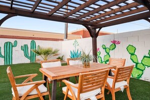 An outdoor patio with a wooden table and chairs, surrounded by a low wall with cactus and plant murals. - Old Town Fiesta 🌵⛳ Heated Pool, Game Room Across from Golf in Scottsdale (Scottsdale)