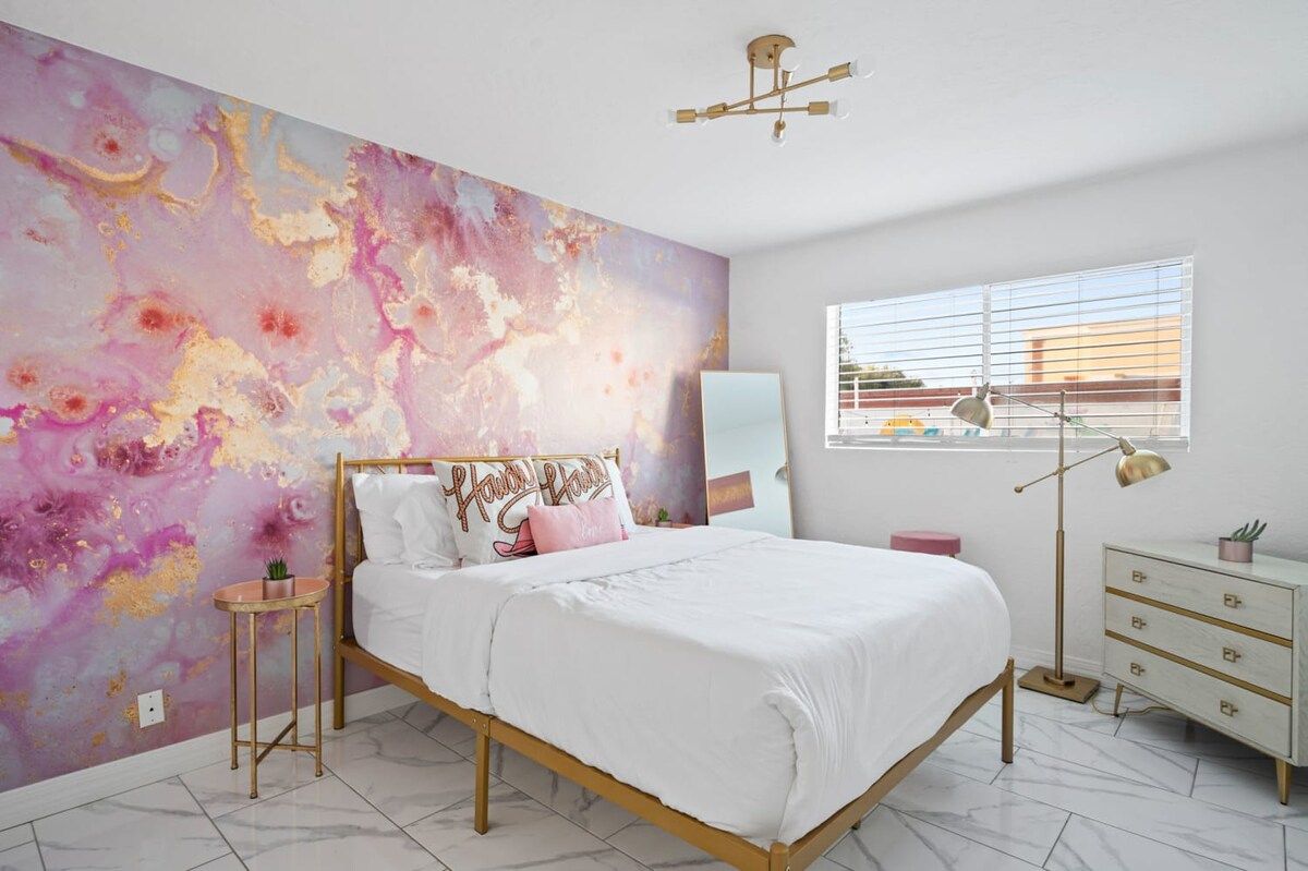 A bedroom with a bed, bedside table, lamp, dresser, and a large abstract painting on the wall.