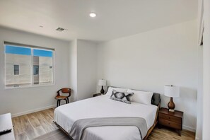 Quarto com uma cama, duas mesas de cabeceira com luminárias, uma cadeira, uma janela com persianas e uma escrivaninha com cadeira.