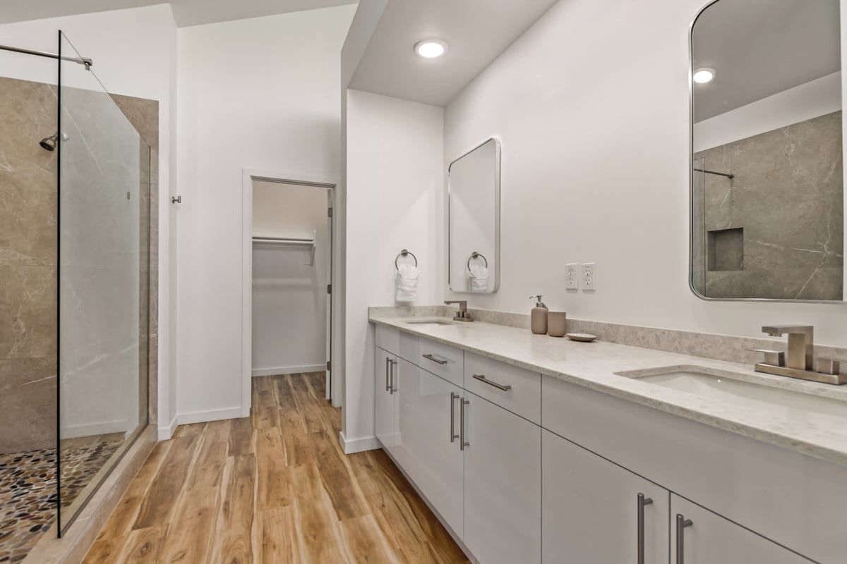 A modern bathroom with a glass shower enclosure, a large mirror, and a vanity with a sink and countertop.