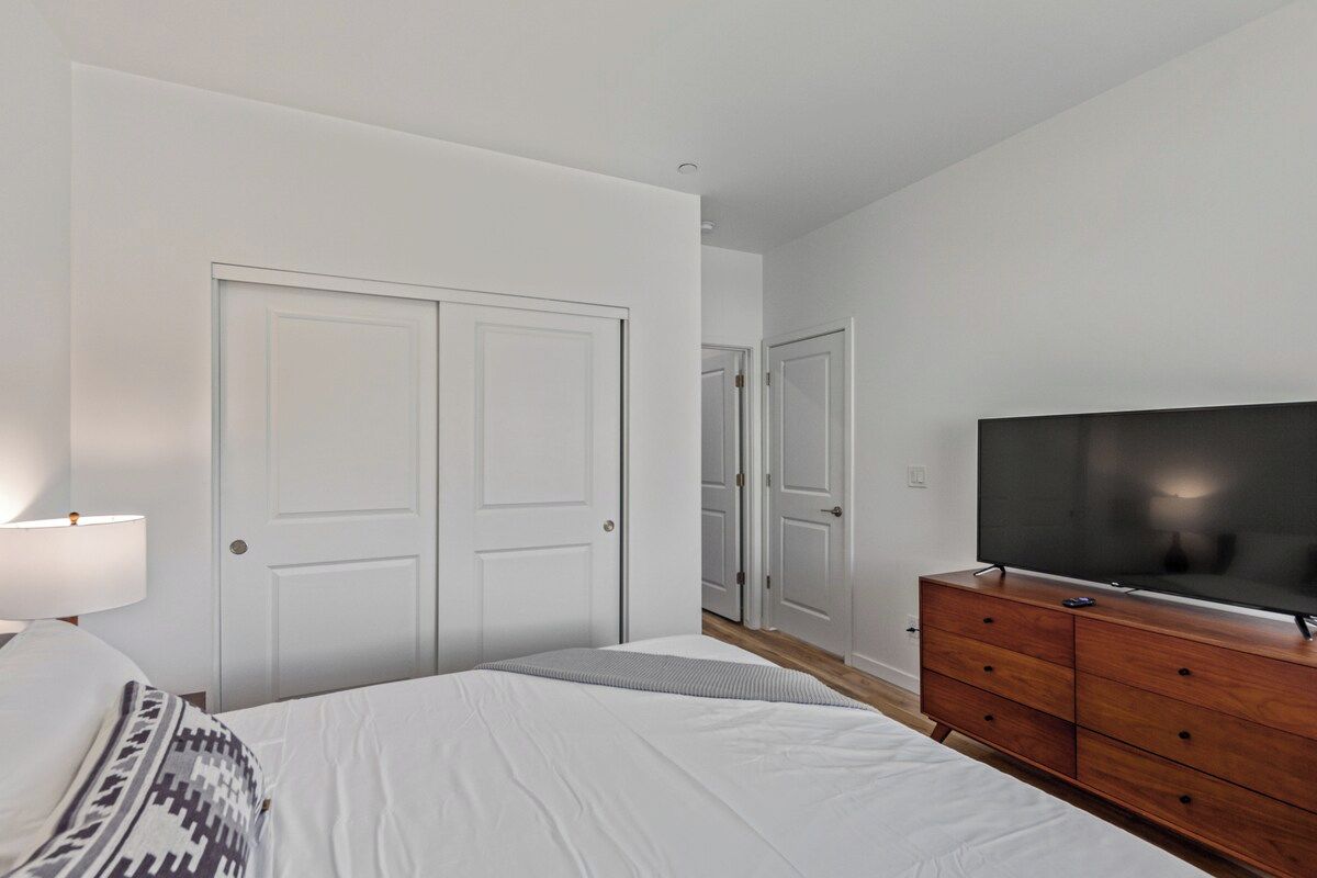 A bedroom with a bed, a dresser, a television, and a door.