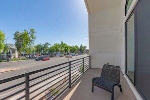 Un balcon avec une chaise, donnant sur une rue bordée d’arbres et où circulent des voitures.