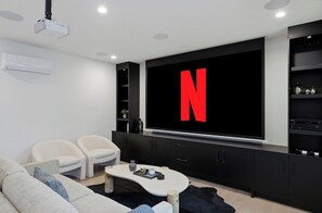 A modern living room with a large flat-screen TV, a sofa, two armchairs, a coffee table, and a black entertainment unit. - The Rowan | $3M Lux | Movie Room, HtdPool, &more! (Phoenix)