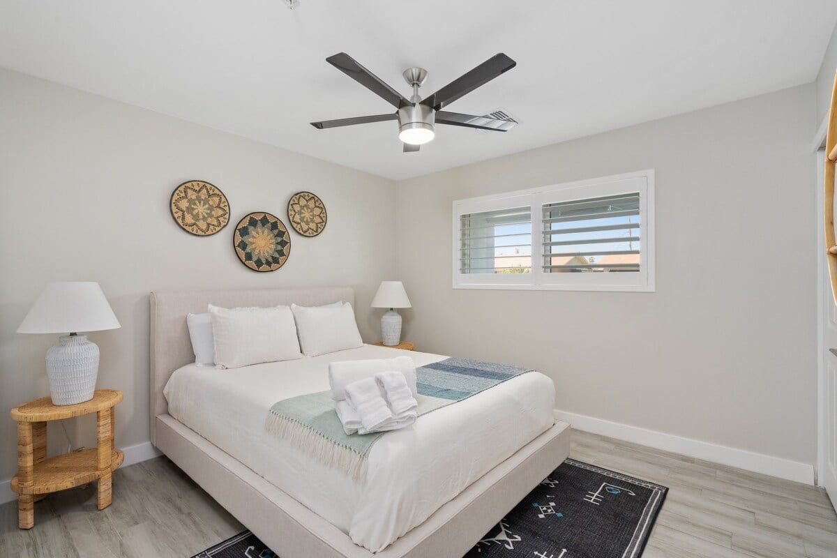 Une chambre à coucher comprenant un lit, deux tables de chevet, un ventilateur de plafond et des éléments décoratifs fixés au mur.