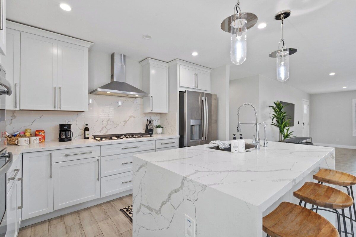 A modern kitchen with white cabinetry, a marble island, stainless steel appliances, and pendant lighting.