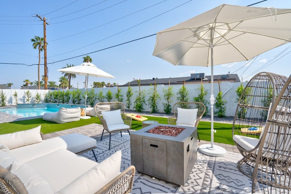 Un espace extérieur aménagé avec une terrasse, une piscine, des chaises longues, un foyer et des parasols.