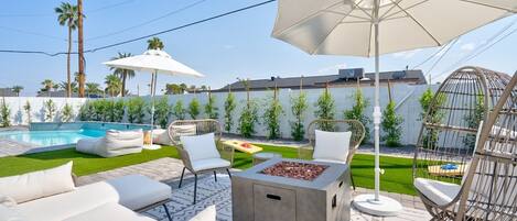Un espace extérieur aménagé avec une terrasse, une piscine, des chaises longues, un foyer et des parasols.