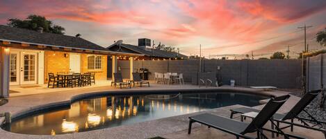 A backyard with a swimming pool, outdoor seating, and a patio area.