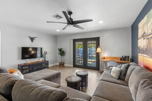 A modern living room with a ceiling fan, a flat-screen TV, a cactus, and a dining area with a lamp. - Scottsdale Retreat with Private Pool | 4BR Home Near Old Town (Scottsdale)