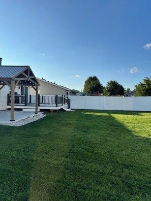 A residential backyard with a covered patio, a white fence, and a well-maintained lawn. - Stateline Family Retreat  (South Beloit)