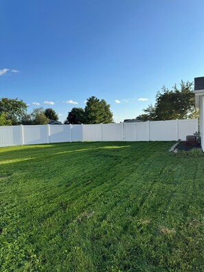 A well-maintained grassy backyard with a white fence and trees in the background. - Stateline Family Retreat  (South Beloit)