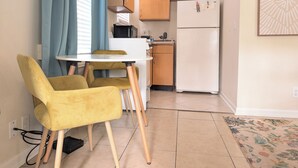 Een compacte keuken met een witte koelkast, houten kastjes en een eettafel met gele stoelen.