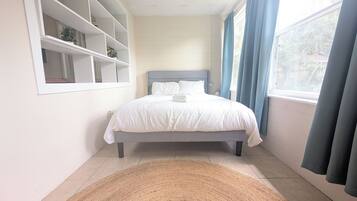 Un dormitorio con una cama, una ventana con cortinas, una estantería y una alfombra.