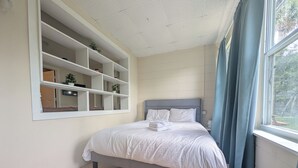 Een slaapkamer met een bed, een inbouwkast, een raam met gordijnen en een kleed.