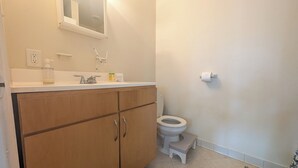 Een badkamer met een houten kastje, een witte wasbak, een toilet en een klein opstapkrukje.
