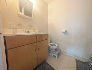 Ein Badezimmer mit einem Holzkabinent, einem weißen Waschbecken, einer Toilette und einer kleinen Stehocker.