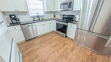 Una cocina moderna con electrodomésticos de acero inoxidable, armarios blancos y piso de madera.