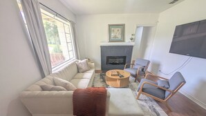 Een woonkamer met een bank, fauteuils, een salontafel, een open haard en een televisie.