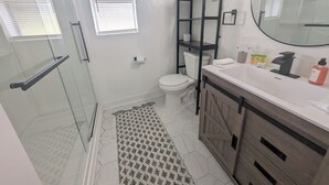 Een badkamer met een douchecabine van glas, een toilet, een wastafel met toiletartikelen en een spiegel.