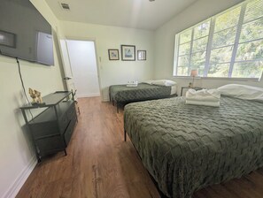 Ein Schlafzimmer mit zwei Betten, einem Fernseher und einem Fenster mit Jalousien.