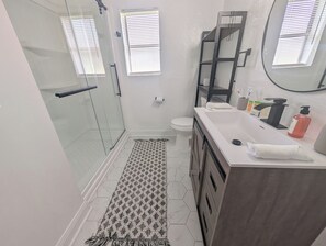 Ein modernes Badezimmer mit einer Duschkabine aus Glas, einer weißen Toilette, einem Waschtisch mit Spiegel und einem gemusterten Teppich auf dem Boden.