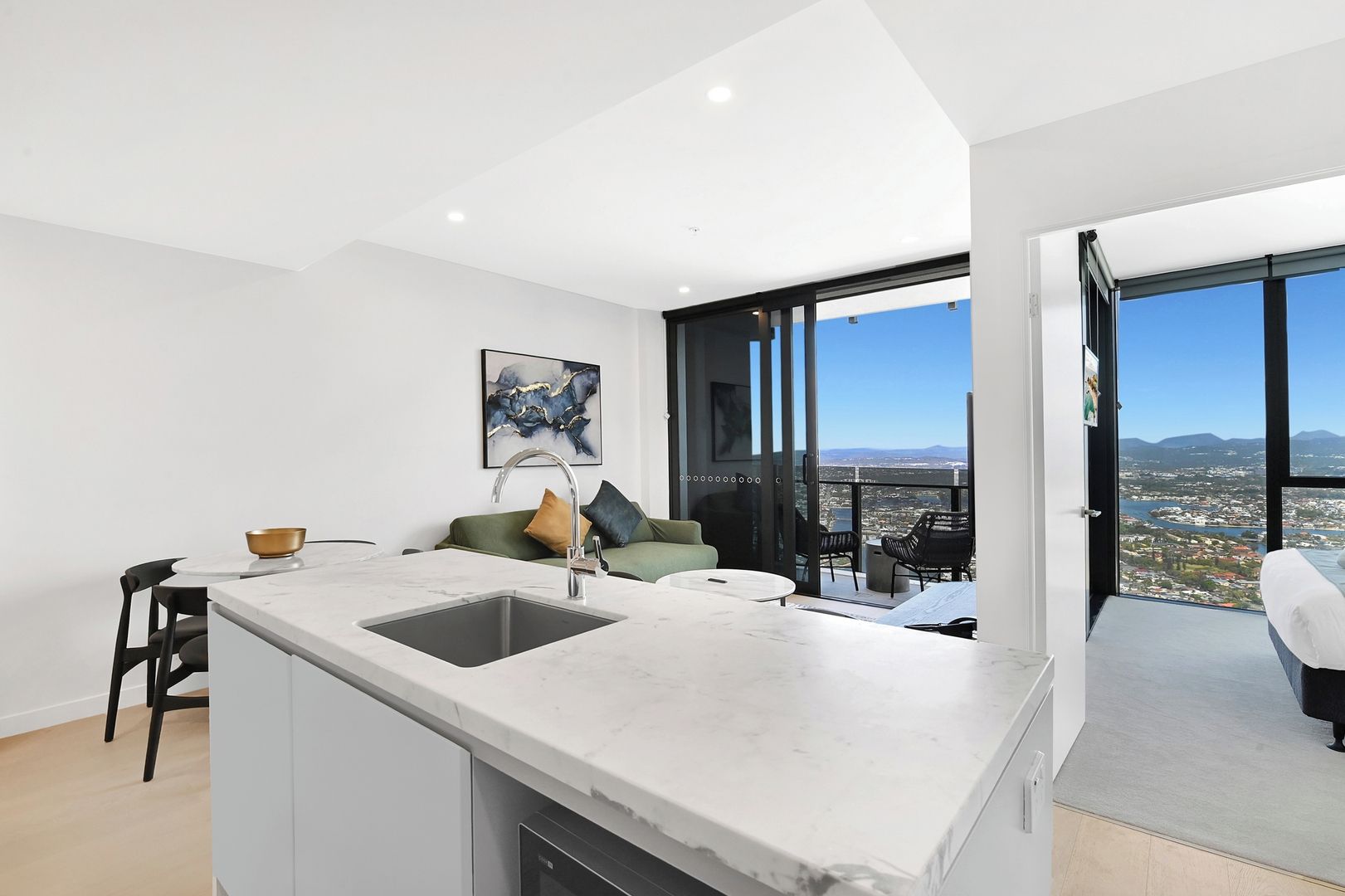 Eine moderne Küche mit einer großen Kochinsel, einem Essbereich mit Tisch und Stühlen, einer Couch mit Kissen sowie ein Balkon mit Blick auf die Stadt.