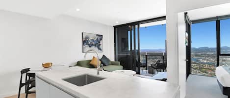 A modern kitchen with a large island, a dining area with a table and chairs, a sofa with cushions, and a balcony with a city view.