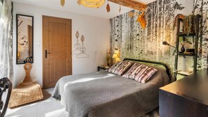 Une chambre avec un lit, une porte en bois, un mur orné de motifs de feuilles, un luminaire suspendu et une étagère avec des plantes.