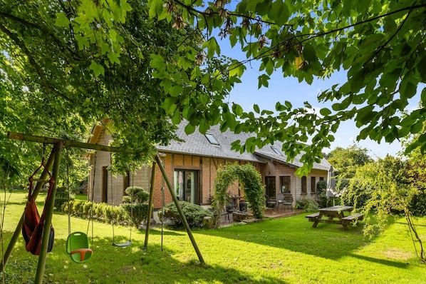Uma casa com fachada de tijolos, um gramado bem cuidado e um balanço.