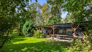 Un chalet rustique en bois, doté d’un porche abrité, entouré d’une végétation luxuriante et d’arbres.