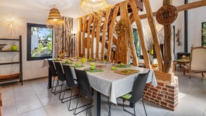 Un espace repas avec une longue table dressée pour le repas, des poutres en bois et des luminaires suspendus.