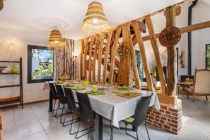 Uma sala de jantar com uma mesa comprida posta para refeição, vigas de madeira e luminárias pendentes.