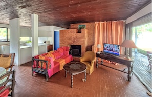 A cozy living area with a brick fireplace, a sofa, a television, and a dining table. - 3 bedroom amazing home in Lacanau (Lacanau)