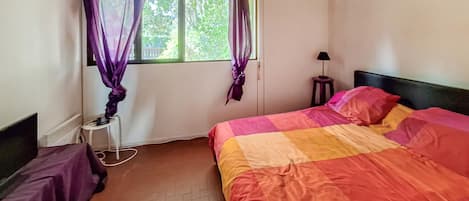 A bedroom with a bed, a window with curtains, a bedside lamp, and a small stool.